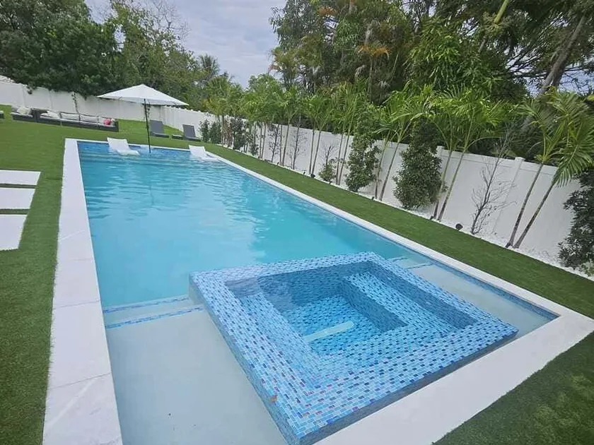 Long lap pool with a raised spa finished in blue glass mosaic, turf surround