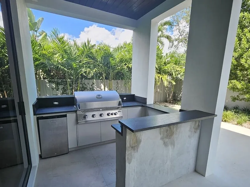 Covered outdoor kitchen with built-in grill, bar counter and dark wood ceiling