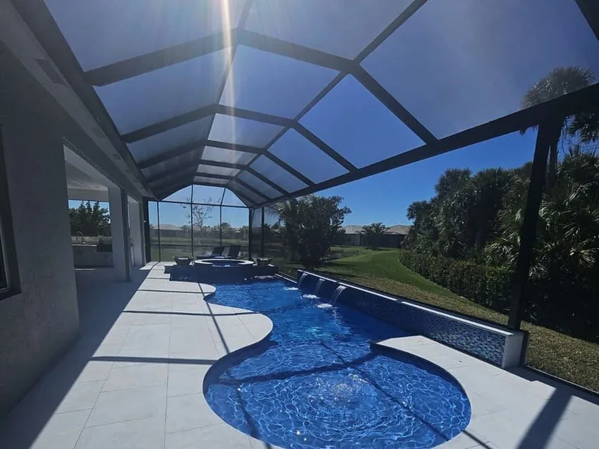Freeform pool and spa inside a screen enclosure with large-format deck tile